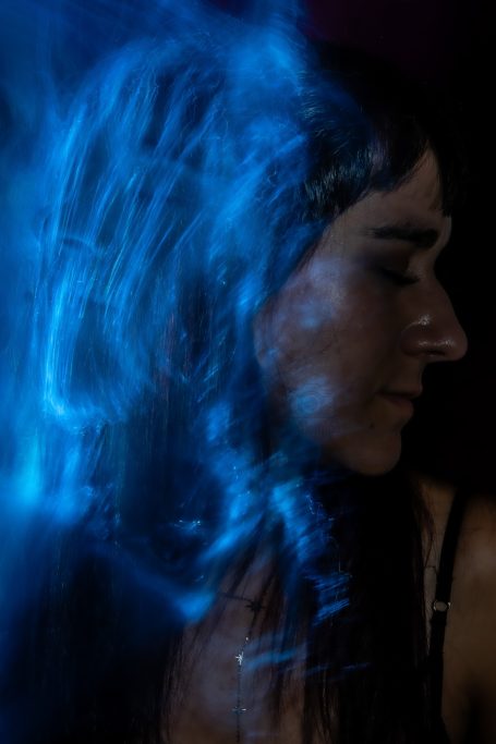 Rostro de Luz Mujer con cabello oscuro, efectos de luz azul y fondo difuso.