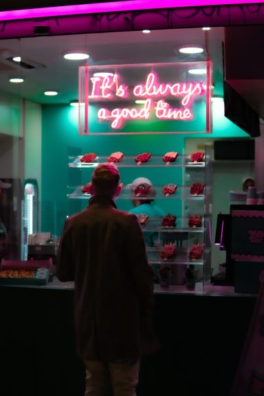 Persona de espaldas frente a un mostrador iluminado con neón y dulces.