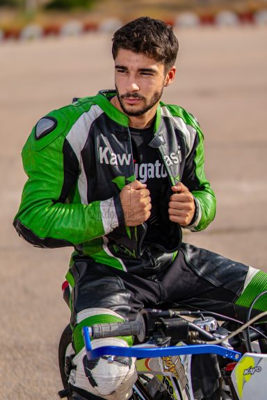 Hombre con traje de motociclismo verde y negro, sentado sobre una motocicleta.