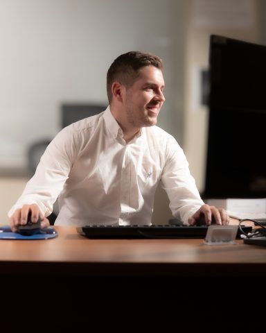 Hombre sonriente en camisa blanca trabajando en un escritorio con computadora.