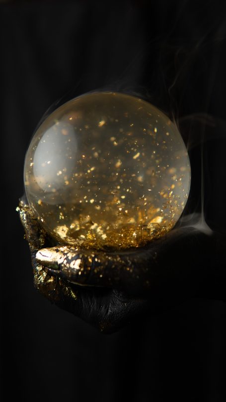 Oro y negro Esfera transparente con partículas doradas dentro, sostenida por una mano oscura.