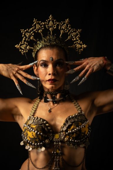 Mujer con adornos elaborados en la cabeza y uñas largas, posando con expresión fuerte.