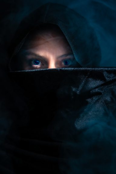 Mujer con rostro parcialmente cubierto, mirando intensamente desde la oscuridad.