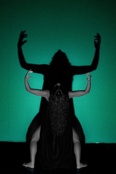 Grito en sombra Sombra de una figura humana con brazos levantados, contra un fondo verde.