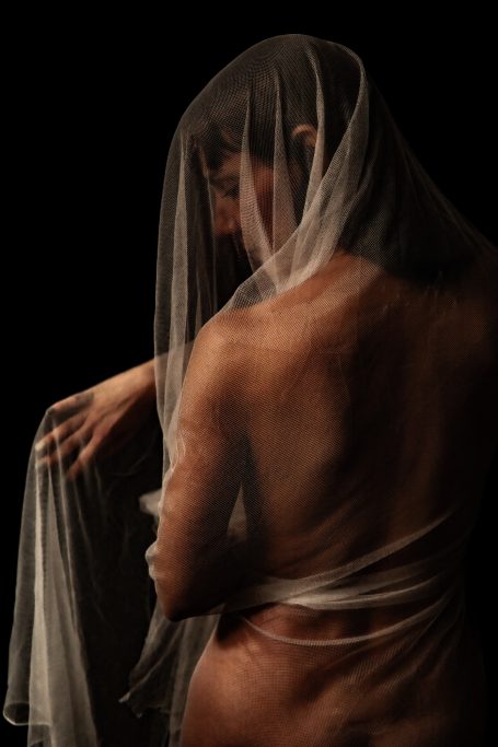 Velo y luz Mujer con velo semitransparente, vista desde atrás, sobre fondo oscuro.