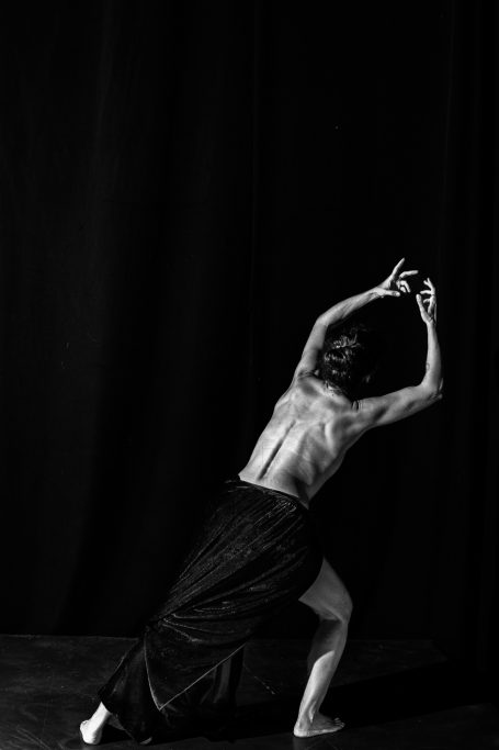 Lamento Persona de espaldas, en movimiento artístico, con fondo oscuro y luz dramática.