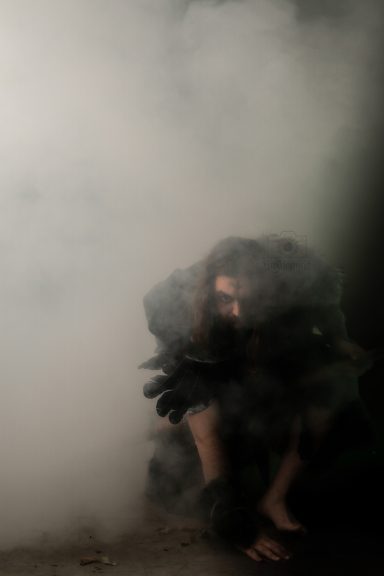 Persona en una esquina, parcialmente oculta por una densa neblina, con una expresión sombría.