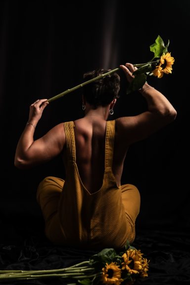 Persona de espaldas con tirantes amarillos y flores, en un entorno oscuro.