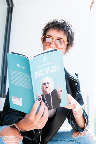Persona con gafas leyendo un libro de portada azul con una figura caricaturesca.