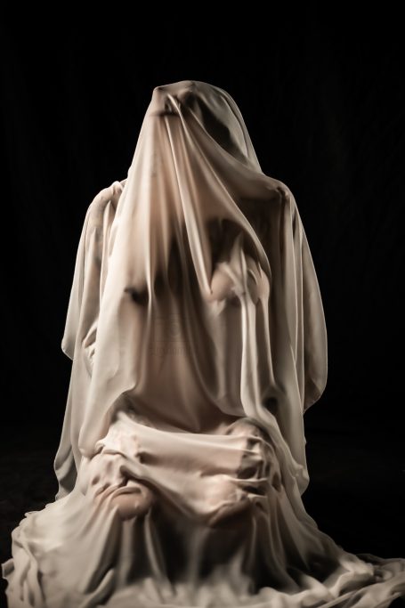 Mármol Figura femenina vestida con una tela translúcida, en una pose introspectiva sobre fondo oscuro.